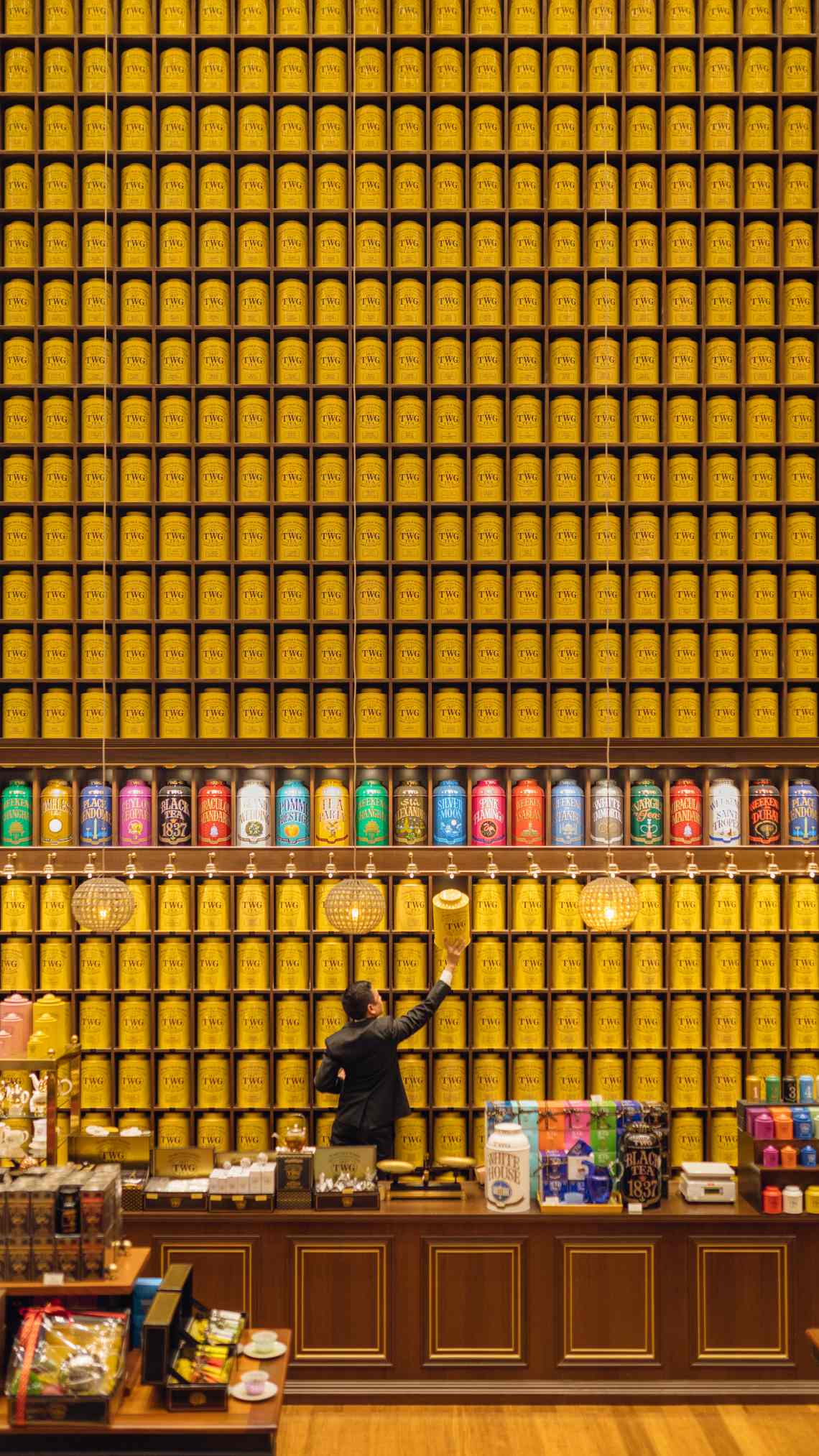 Man reaching out for a tea canister from a large high wall lined with tins